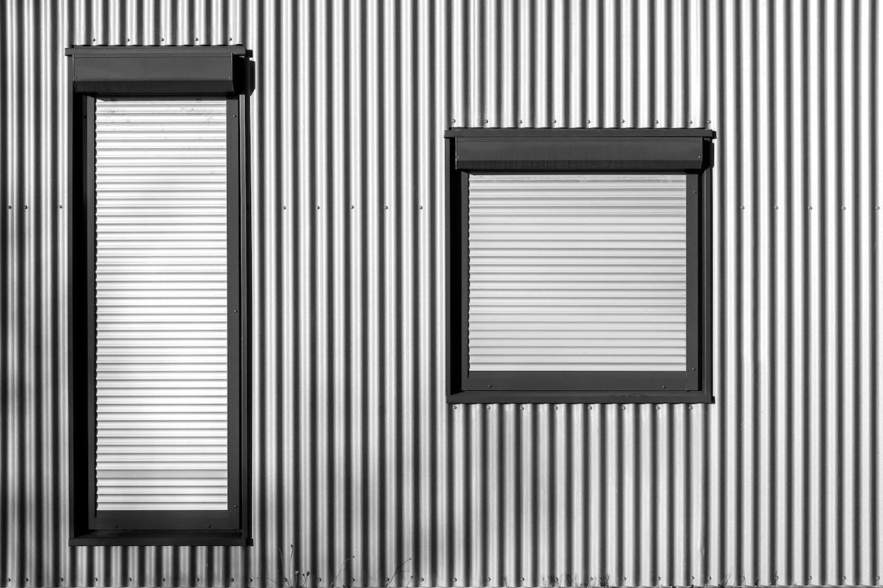 Monochromatic image of a sleek industrial building facade featuring closed metal shutters and corrugated texture.